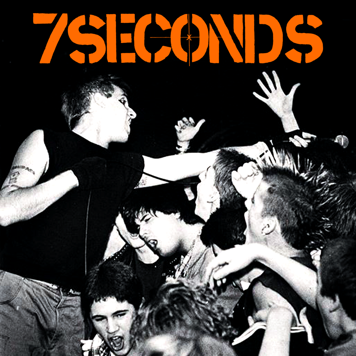 A punk band singer reaches into a crowd of energetic fans at a concert, with 7SECONDS in bold orange text above them. Black and white photo with high energy and raised hands.