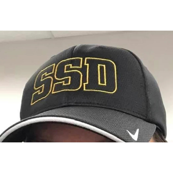 A black SS Decontrol DriFIT hat with yellow outlined SSD letters on the front, white Nike logo on the bill, and made from moisture-wicking polyester knit mesh. Only the top of the person’s head is visible.