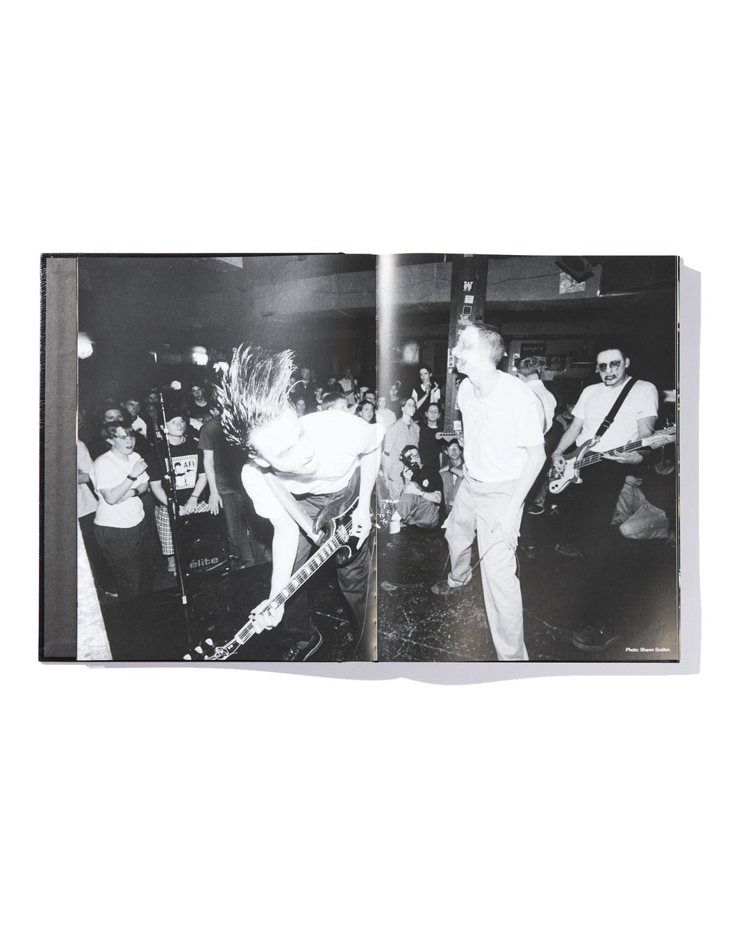 Black-and-white photo of The Almighty Jeremy Dean Erik Bader’s punk rock band performing on stage, featuring energetic musicians playing guitar and singing while a crowd watches closely in the background—an iconic moment from music history, captured as exclusive limited edition memorabilia by Ink & Dagger, perfect for fans and collectors of the brand.