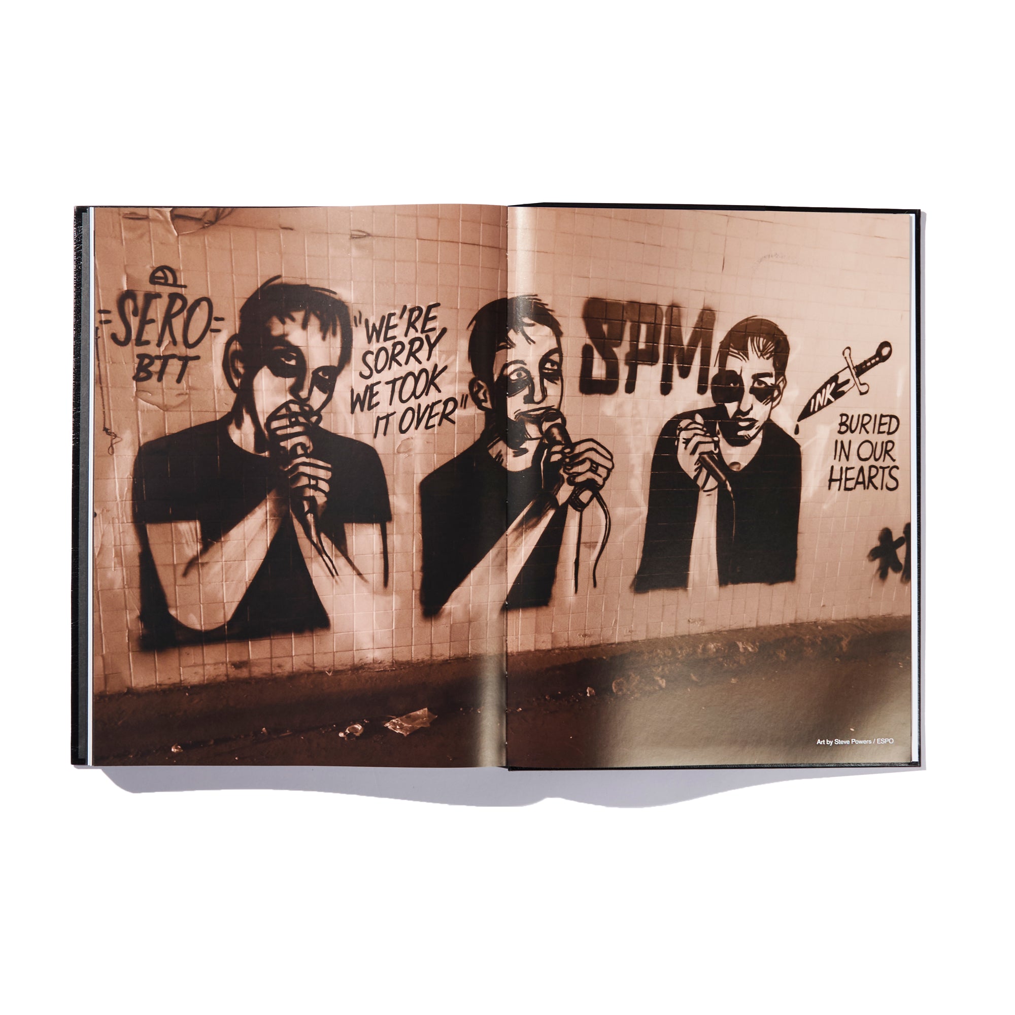 A book spread from the Ink & Dagger limited edition hardcover showcases graffiti art of three people holding microphones. Above them, bold text reads SERO BTT, We're sorry we took it over, SPM, and Buried in our hearts—offering a powerful visual tribute worthy of The Almighty Jeremy Dean Erik Bader.