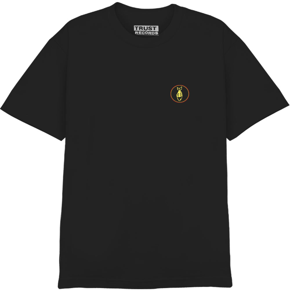 A black Fishbone Comfort Colors T-shirt featuring a small circular yellow and red ant logo on the left chest and a Trust Records label inside the collar.