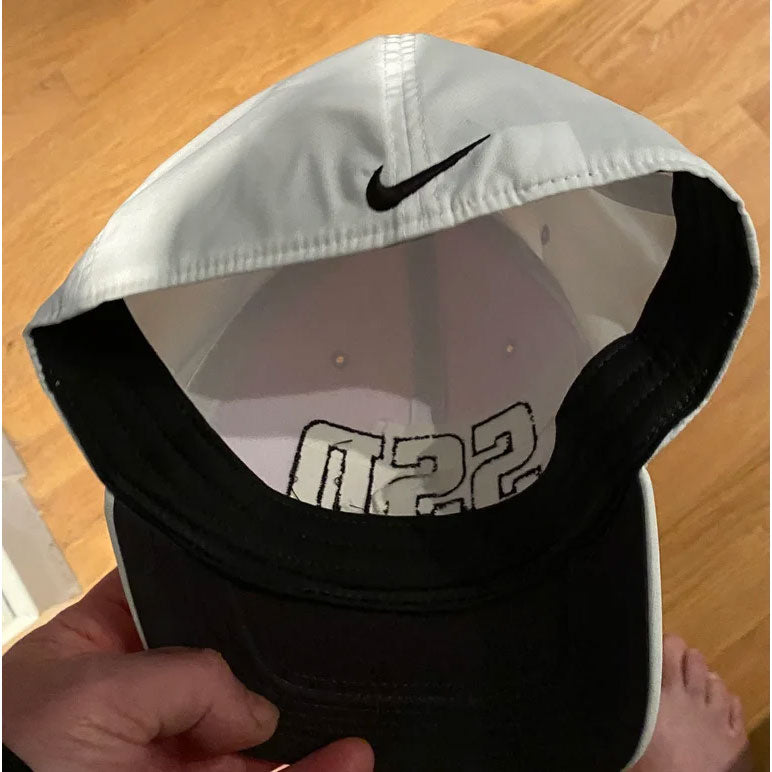 A SS Decontrol Classic 99 white baseball cap by Nike, with bold black SSDecontrol letters embroidered on the front, AeroBill and Dri-FIT tech, held by hand over a wooden floor.