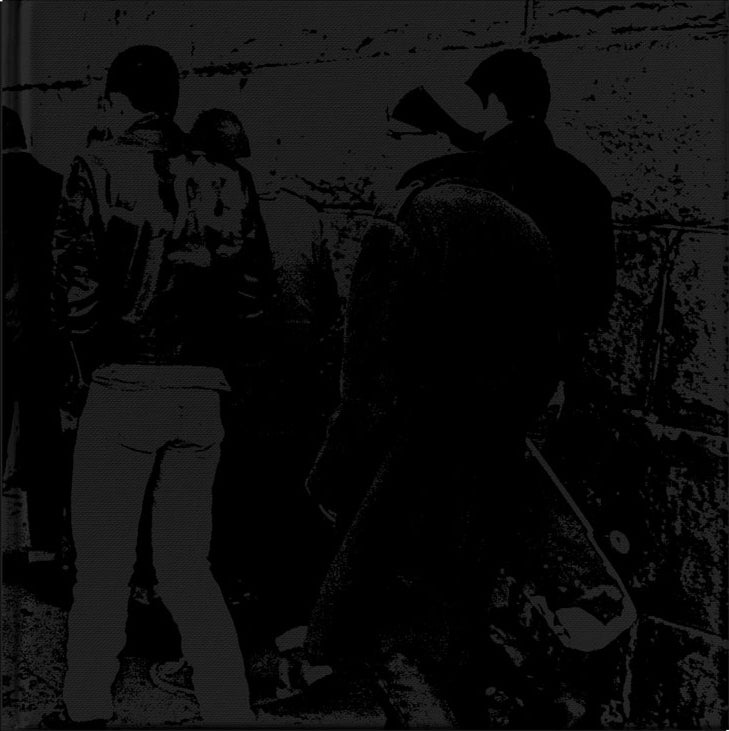 A group stands closely together facing a wall, some with backs turned. One wears a leather jacket, another holds a guitar case. This high-contrast black and white image is from SS Decontrol’s Art Compilation Book with exclusive band commentary.