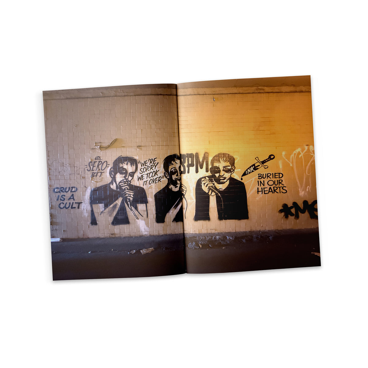 An open Trust Records magazine, issue 4, printed on uncoated paper, shows graffiti art with two stenciled faces, text like “We’re sorry we took it over” and “Buried in our hearts,” plus a syringe near the second face.