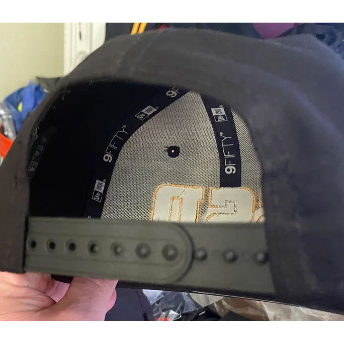 A black SS Decontrol snapback cap with a flat bill, bold yellow SSD embroidery on the front, and an adjustable fit. A shiny sticker accents the brim as a hand holds it.