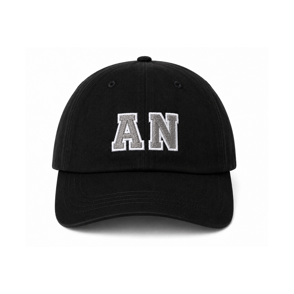 A black twill cap by American Nightmare with white embroidered "AN" letters on the front, displayed against a white background. It features an adjustable fit with a brass clasp closure.