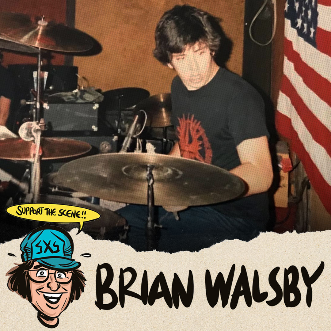 A man plays drums behind a drum kit, wearing a black t-shirt, in a room with an American flag on the wall. A cartoon character with a teal hat and speech bubble saying Support the scene!! appears at the bottom with the text Brian Walsby.
