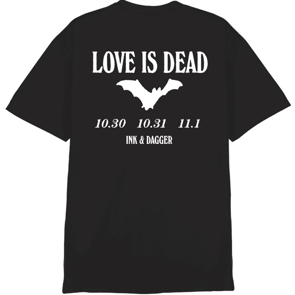A black Ink & Dagger Comfort Colors tee featuring bold white "LOVE IS DEAD" text over a bat, with dates 10.30 10.31 11.1 and INK & DAGGER below—perfect for fans of eye-catching prints.