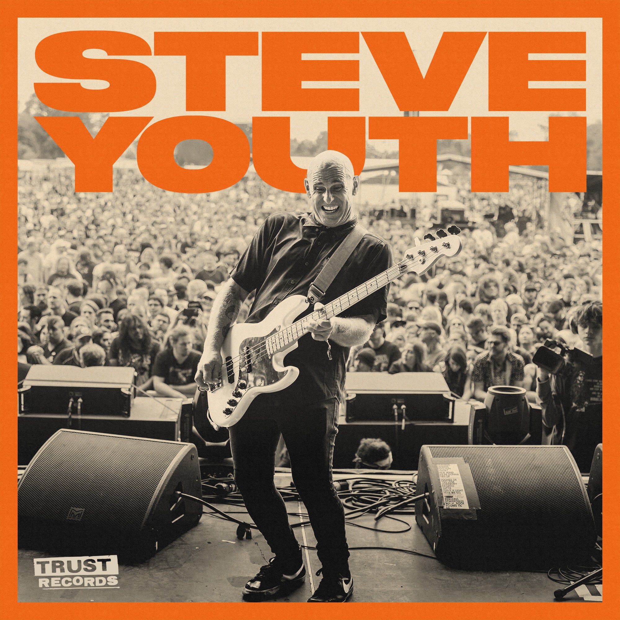 A bald musician playing a guitar smiles energetically on stage in front of a large outdoor crowd. Bold orange text above reads “STEVE YOUTH.” The Trust Records logo is in the bottom left corner.