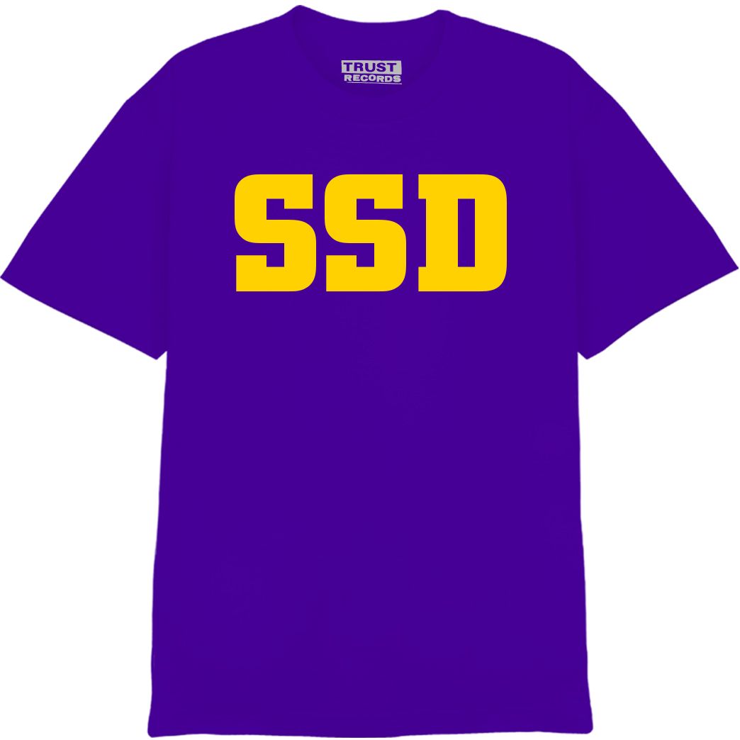 A 100% cotton purple SS Decontrol Alstyle 1301 T-shirt with large yellow SSD letters silkscreened on the front; collar tag reads TRUST RECORDS.