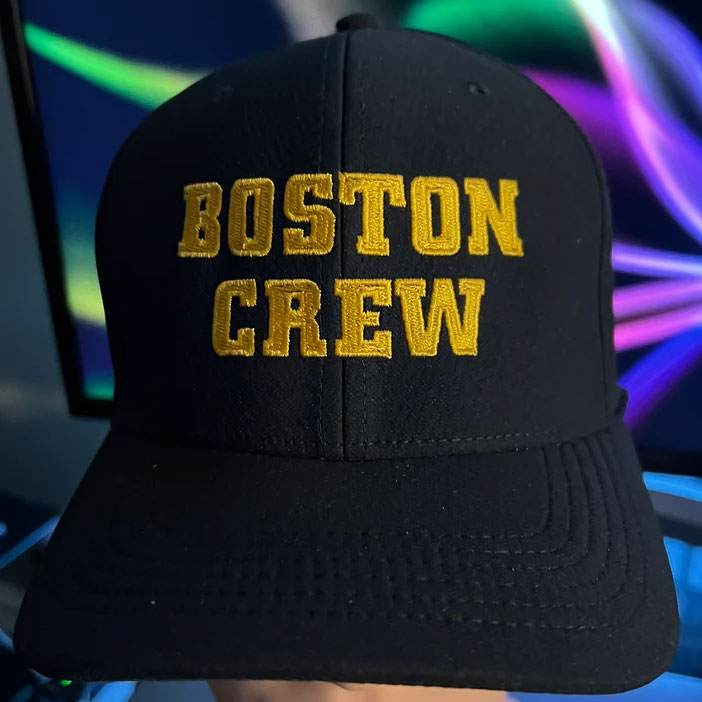 This lightweight black baseball cap by SS Decontrol features yellow embroidered BOSTON CREW text, shown against a colorful blurred background.