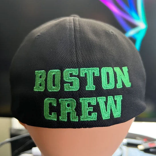 A SS Decontrol Flexfit Baseball Hat with bold green “SSD” embroidery on the front. Two stickers display the Flexfit logo and Cool & Dry Technology, with a blurred computer screen in the background for a modern vibe.