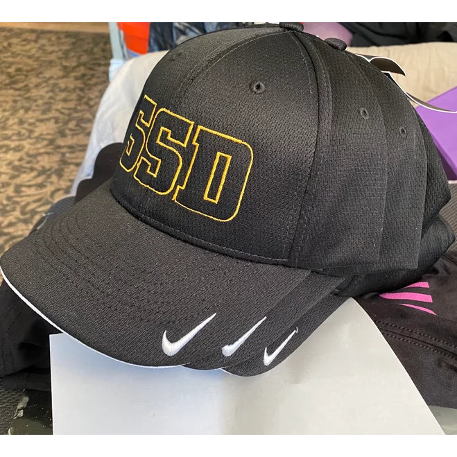 A black SS Decontrol DriFIT hat with yellow outlined SSD letters on the front, white Nike logo on the bill, and made from moisture-wicking polyester knit mesh. Only the top of the person’s head is visible.