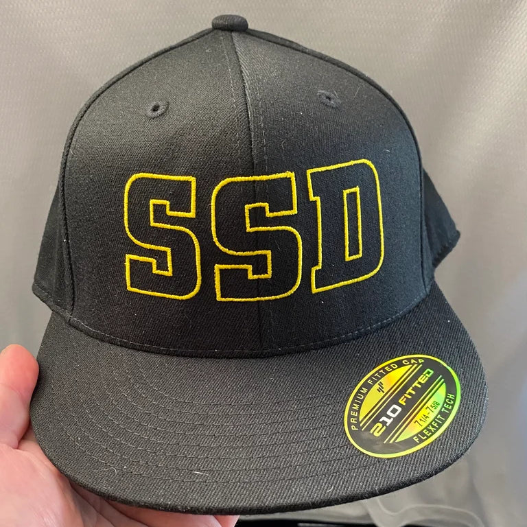 A black six-panel SS Decontrol Flexfit Flat Bill Cap with bold yellow outlined SSD embroidery on the front and a premium fitted 210 Flexfit sticker on the brim.
