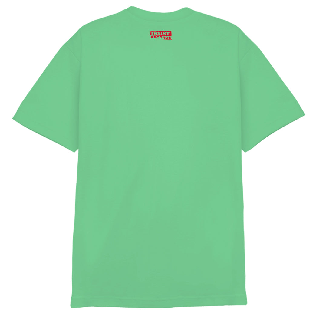 A plain mint green 7 Seconds Alstyle 1301 T-shirt, shown from the back, has a small red label with "TRUST RECORDS" in white near the neckline. Made from 100% cotton and finished with silkscreened details.