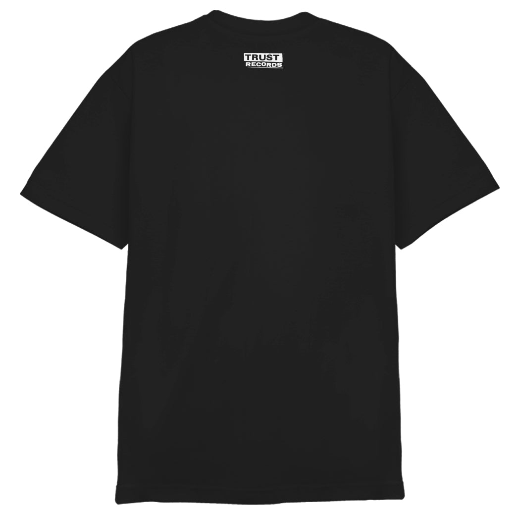 A plain black 100% cotton Circle Jerks Alstyle 1301 T-shirt shown from the back, featuring a small white silkscreened Trust Records logo centered near the neckline.