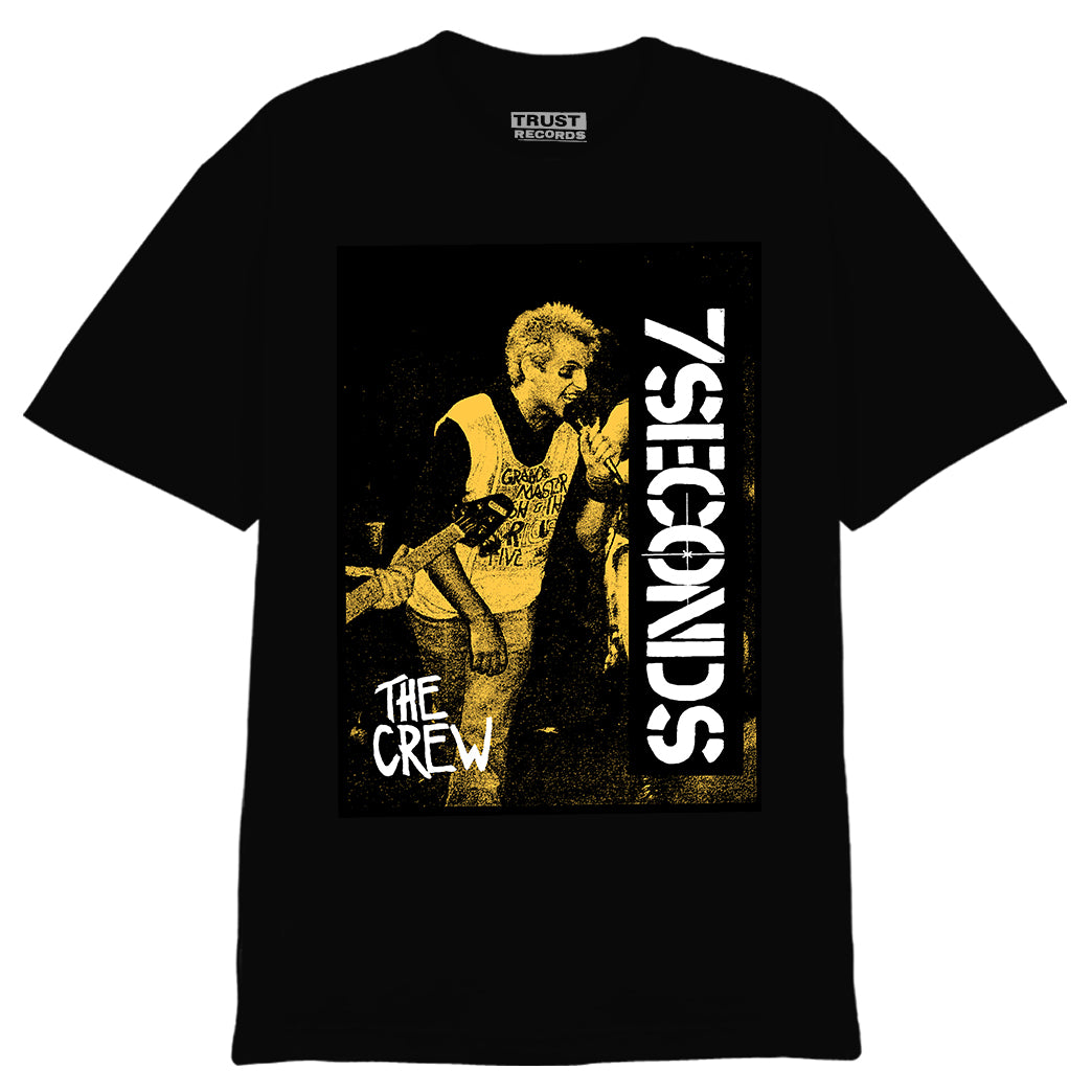 A black 7 Seconds Alstyle 1301 Cotton T-Shirt with a yellow-hued punk singer print, 7SECONDS and THE CREW in white, and an inside collar TRUST RECORDS label.