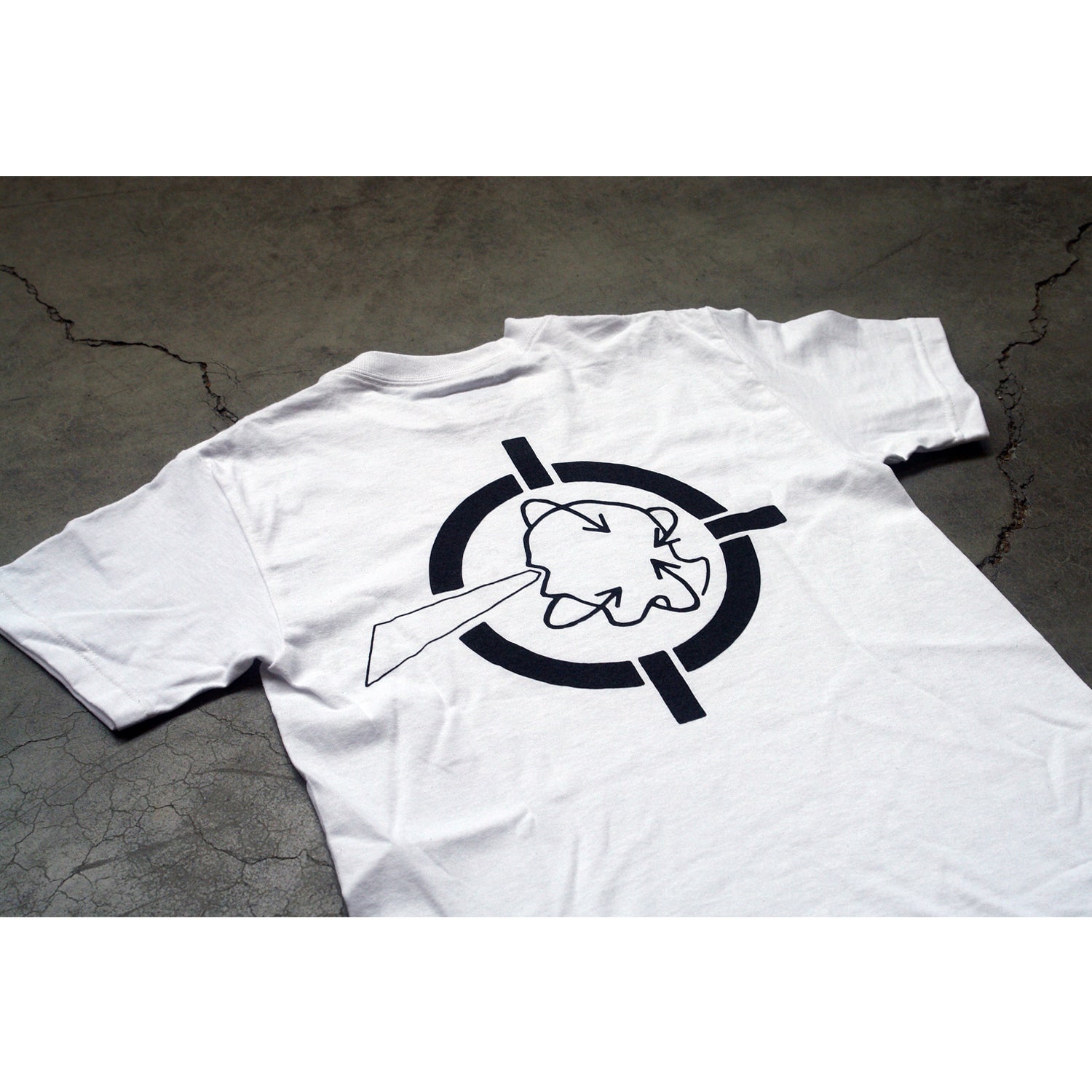 A white Better Youth Organization cotton T-shirt lies on cracked concrete. The back displays a black silkscreened circular target with a bold arrow through a cloud outlined in black.