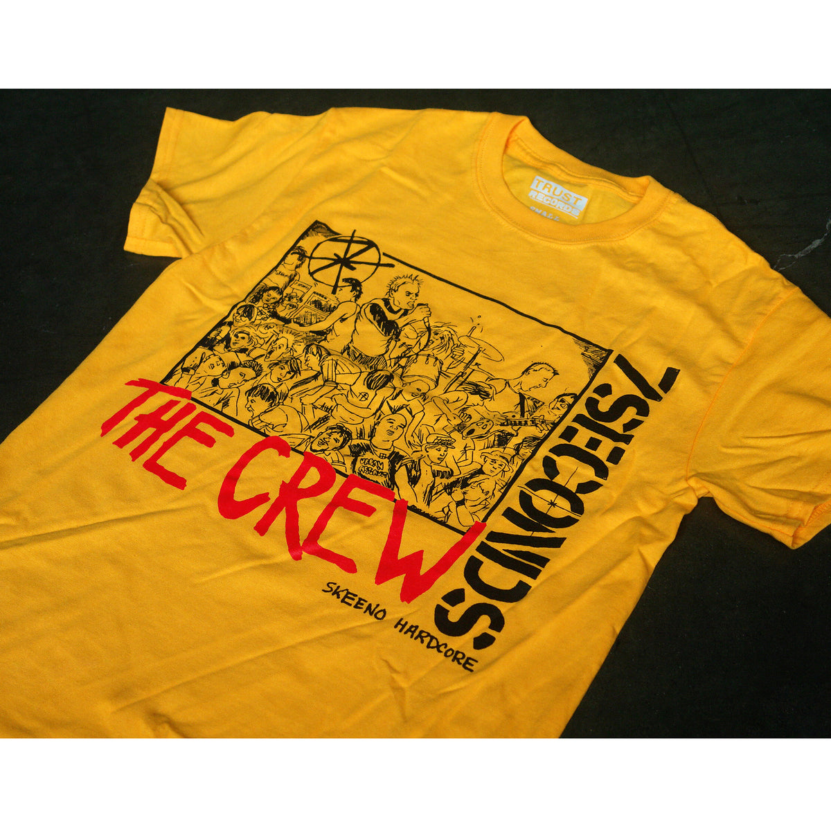 A yellow Alstyle 1301 T-shirt from 7 Seconds with bold black and red silkscreened graphics—THE CREW and 7SECONDS in large letters above a crowd illustration, with SKENO HARDCORE below.