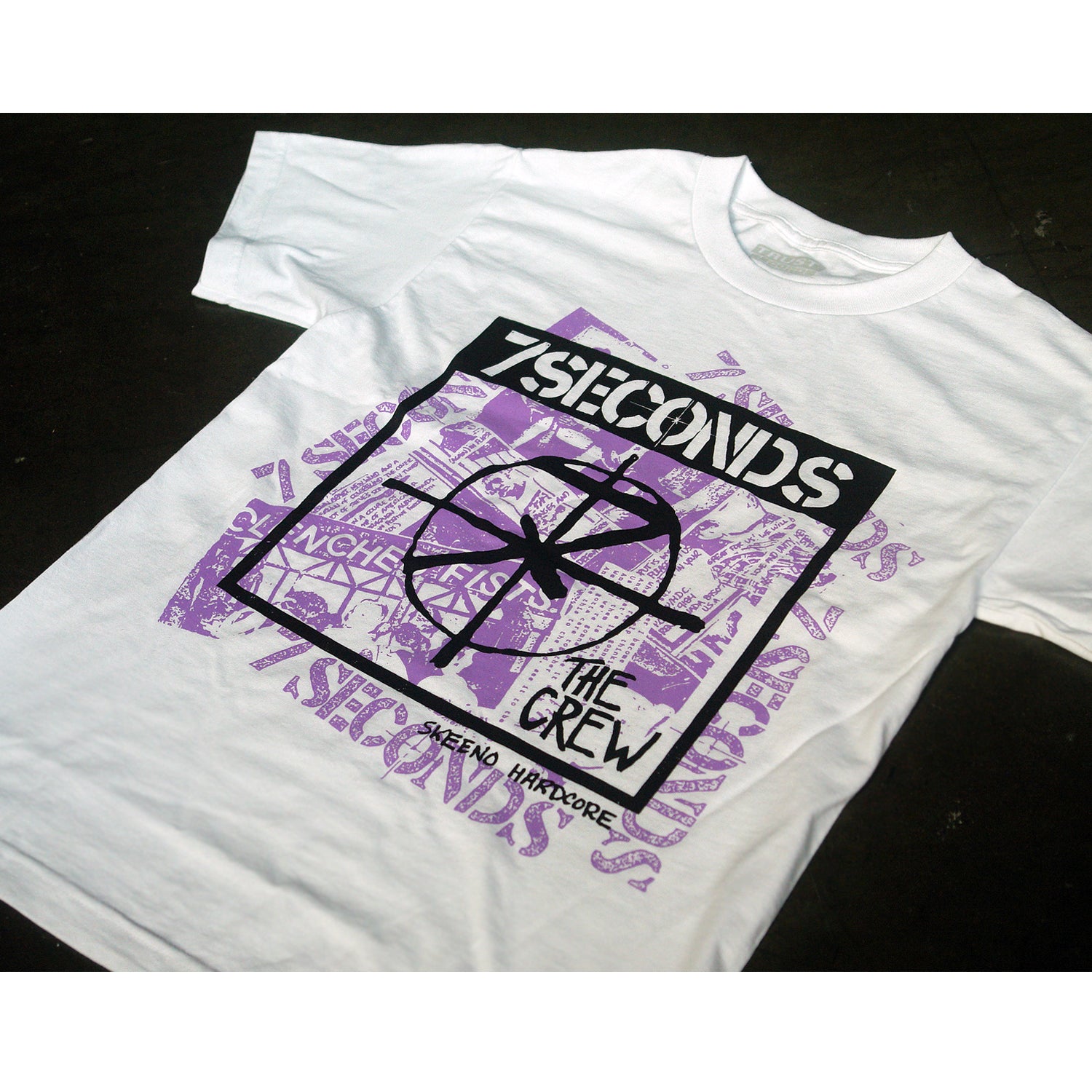A white 100% cotton Alstyle 1301 T-shirt by 7 Seconds, featuring a black and purple silkscreened graphic with “7 Seconds,” “The Crew,” and “Reno Hardcore” text over abstract band-related images.