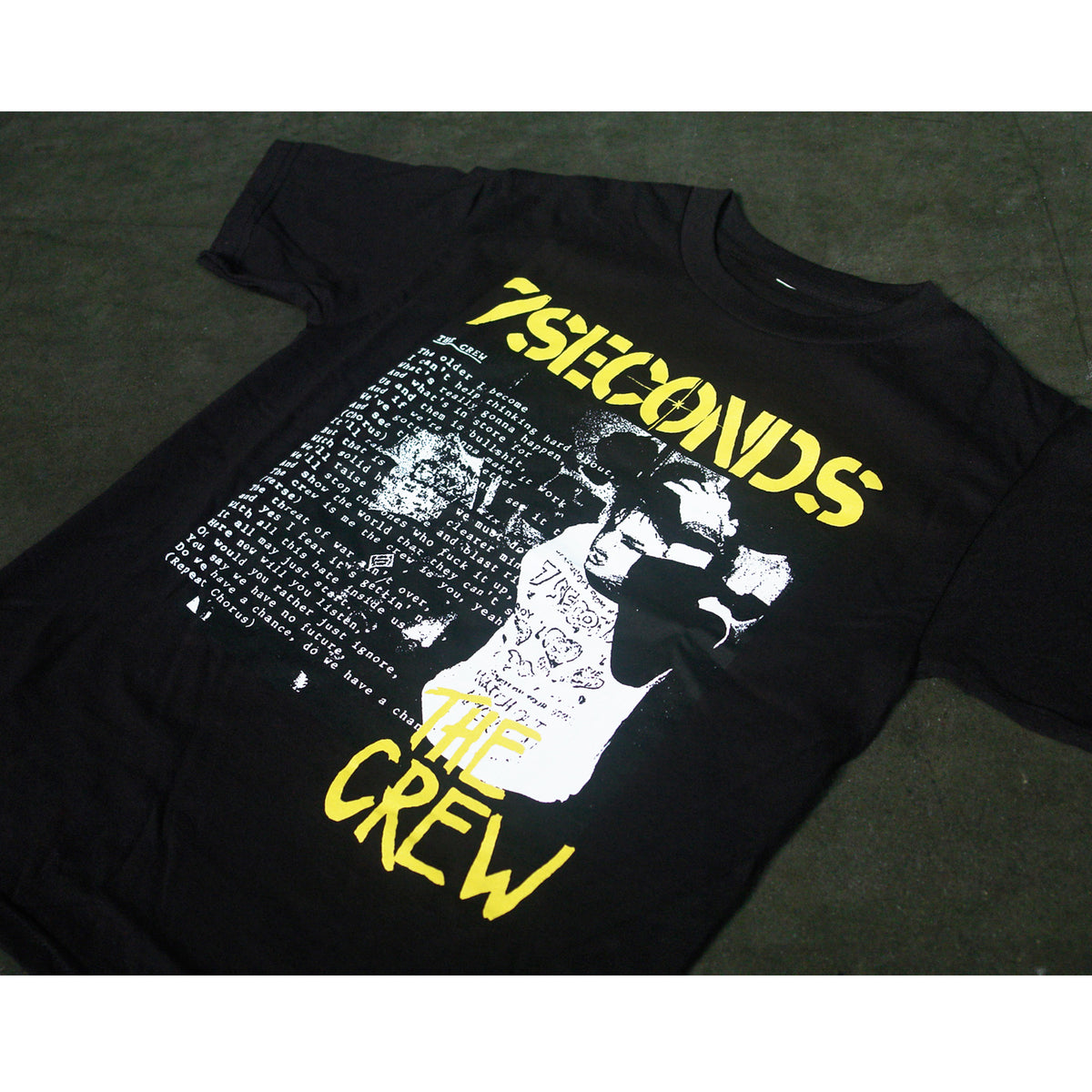 A black 100% cotton Alstyle 1301 T-shirt by 7 Seconds, featuring silkscreened yellow and white 7SECONDS THE CREW graphics of a band performing and a list of song titles or lyrics on the front.