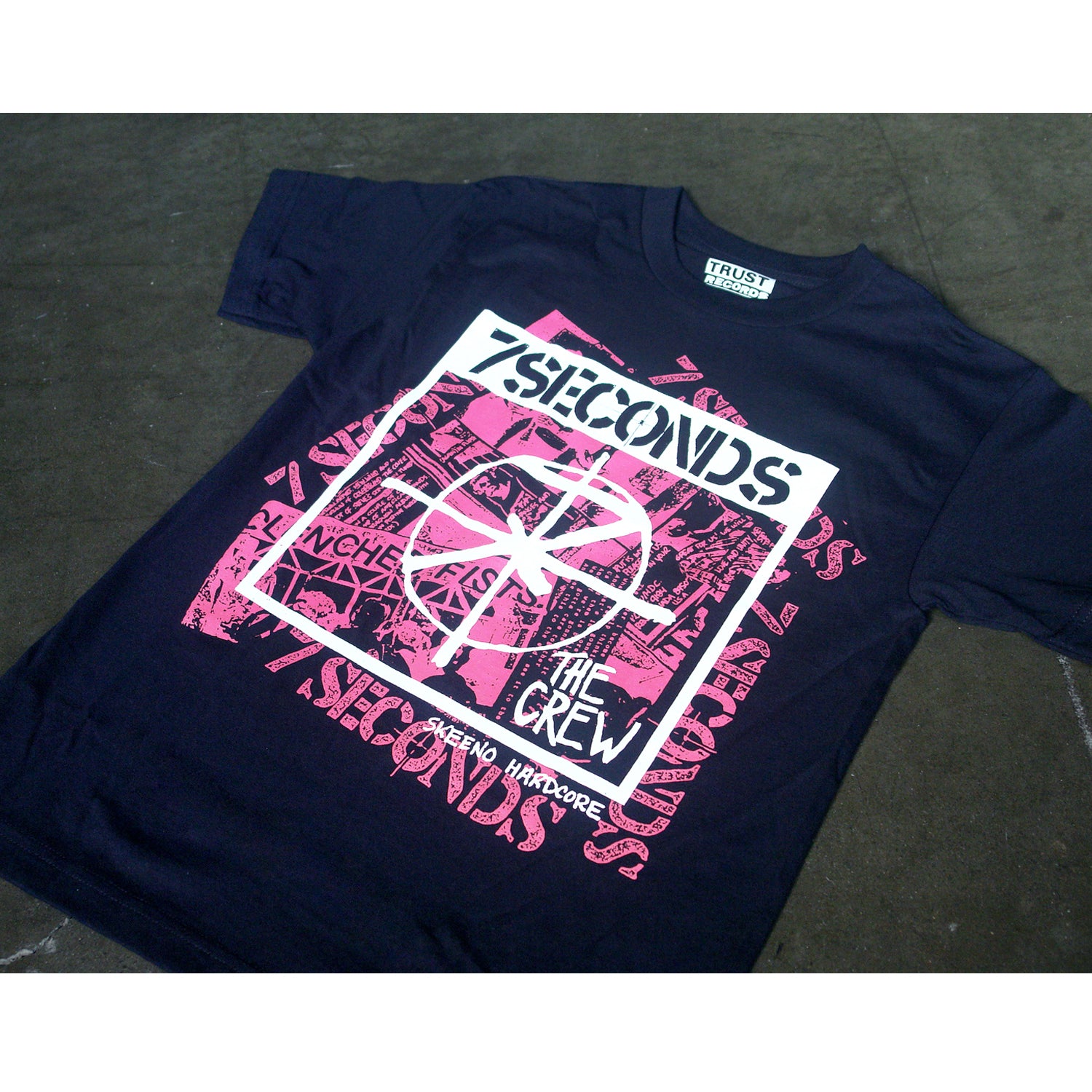 A black 100% cotton Alstyle 1301 T-shirt by 7 Seconds, with pink and white silkscreened graphics featuring 7 SECONDS, THE CREW, RENO HARDCORE, and abstract designs on the front.