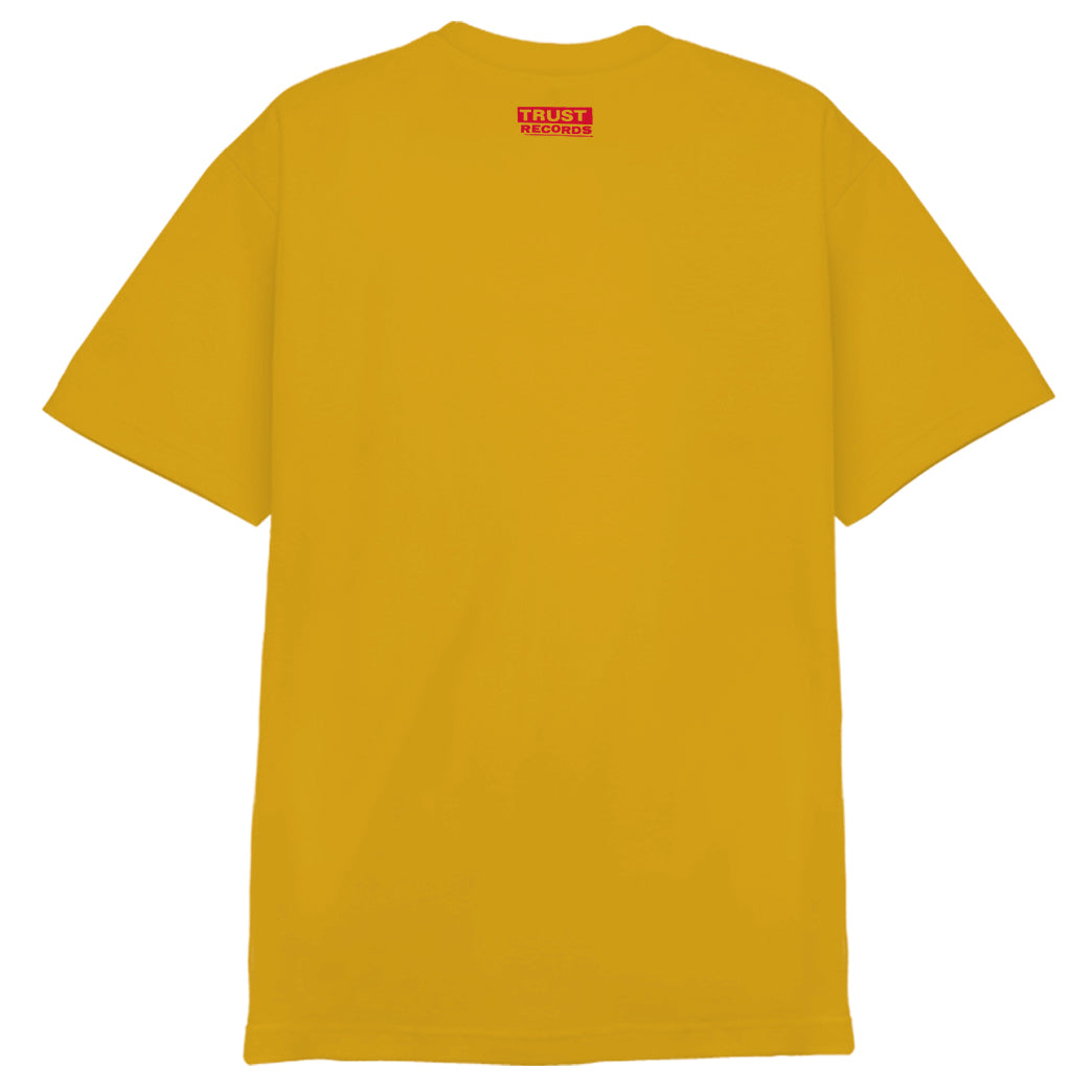 A yellow 7 Seconds Alstyle 1301 T-shirt, 100% cotton, with silkscreened black and red crowd artwork and the text 7 SECONDS, THE CREW, and SCENE/HC HARDCORE on the front. Trust Records branding is on the inside collar.