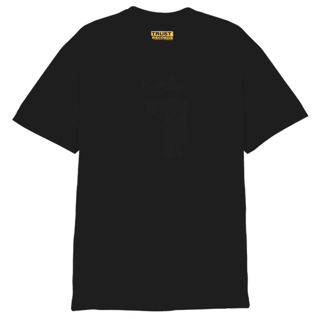Black 7 Seconds Alstyle 1301 T-shirt with a black-and-white photo of a person wearing headphones, yellow 7SECONDS and THE CREW text, silkscreened white lyrics on the front, and TRUST RECORDS printed inside the collar.